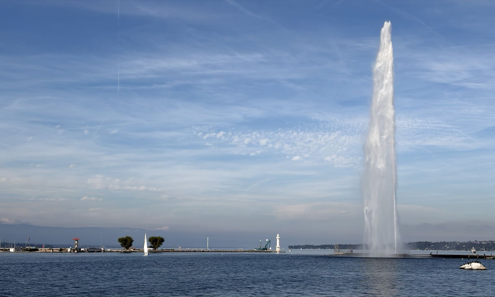 An outrageously large stream of water jets out of a lake. There are a number of boats on the water.