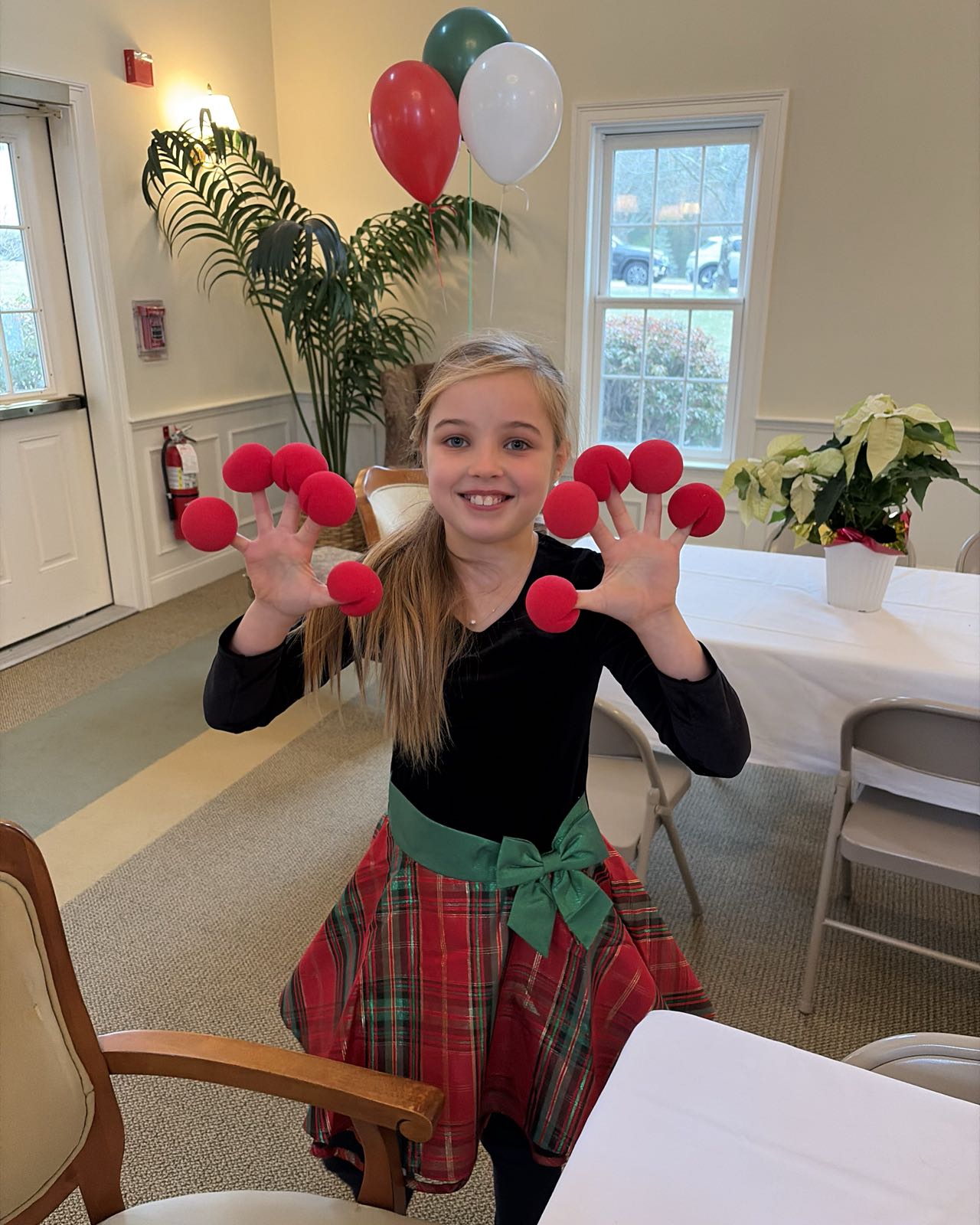 A child in a festive dress has red clown noses on each of her fingers.