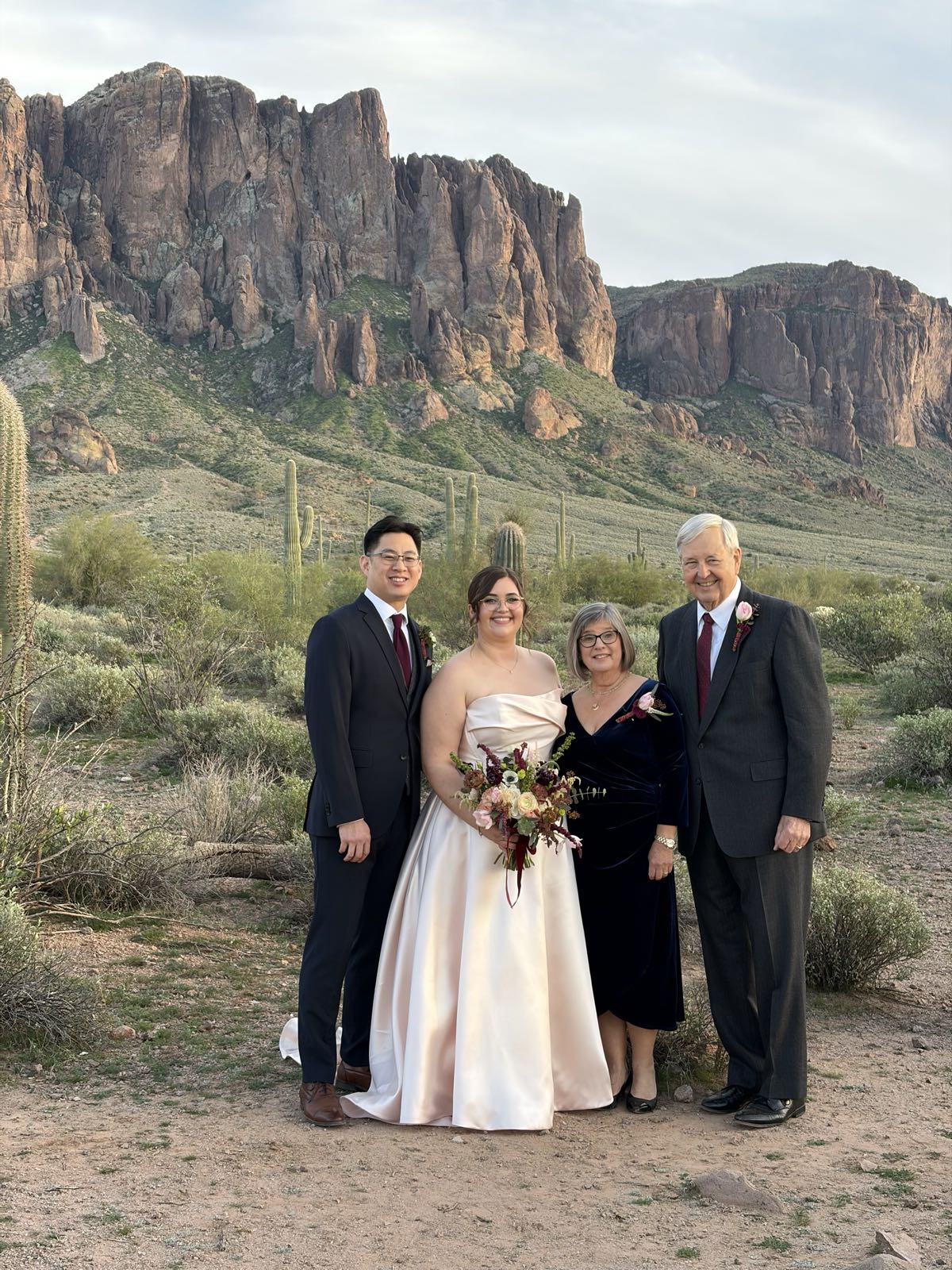 A groom and bride pose with the bride’s parents. Behind them is a beautiful desert backdrop, with a craggy mountain behind it all.