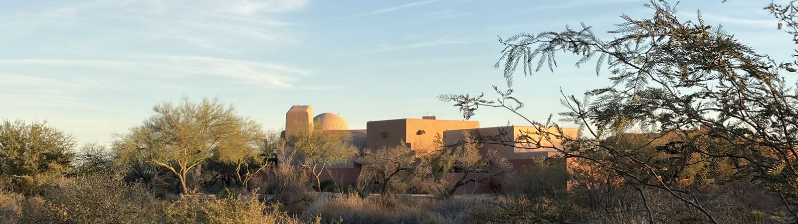 A sand-colored collection of buildings stands in the desert. One of the buildings is domed.