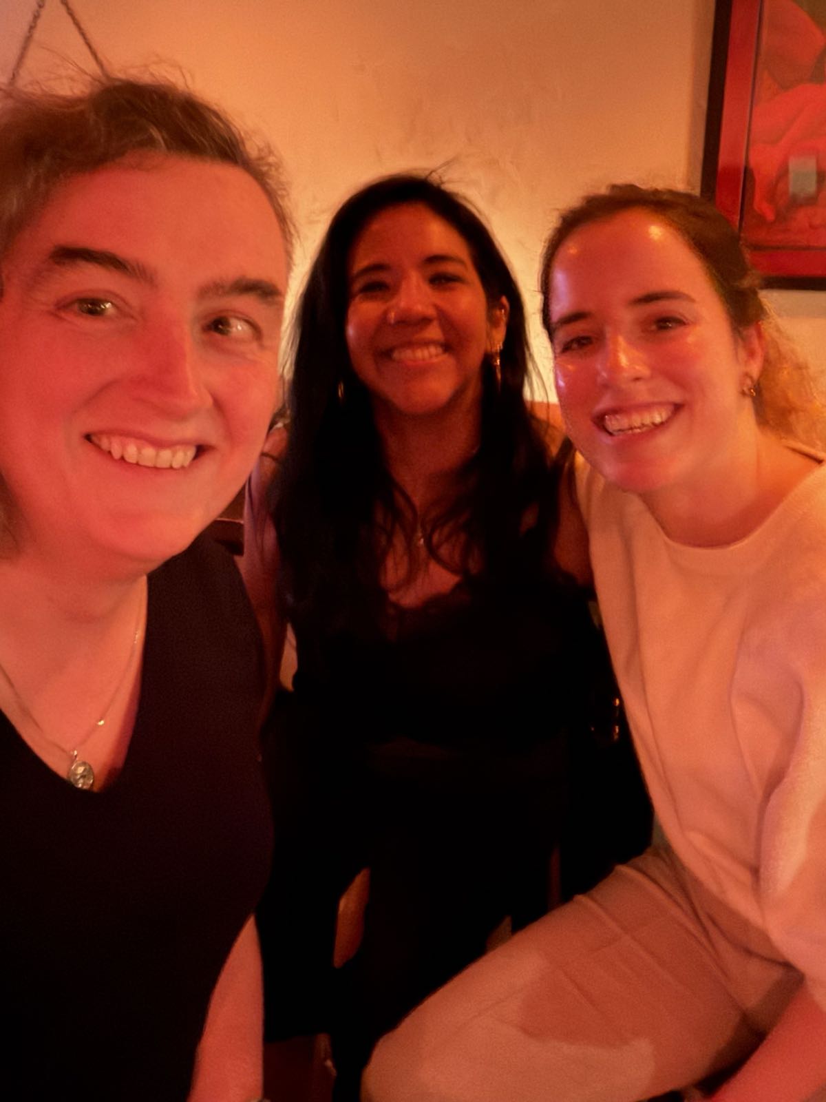 Three women smile for the camera. The lighting in the room has caused everything in the photo to be suffused with redness.
