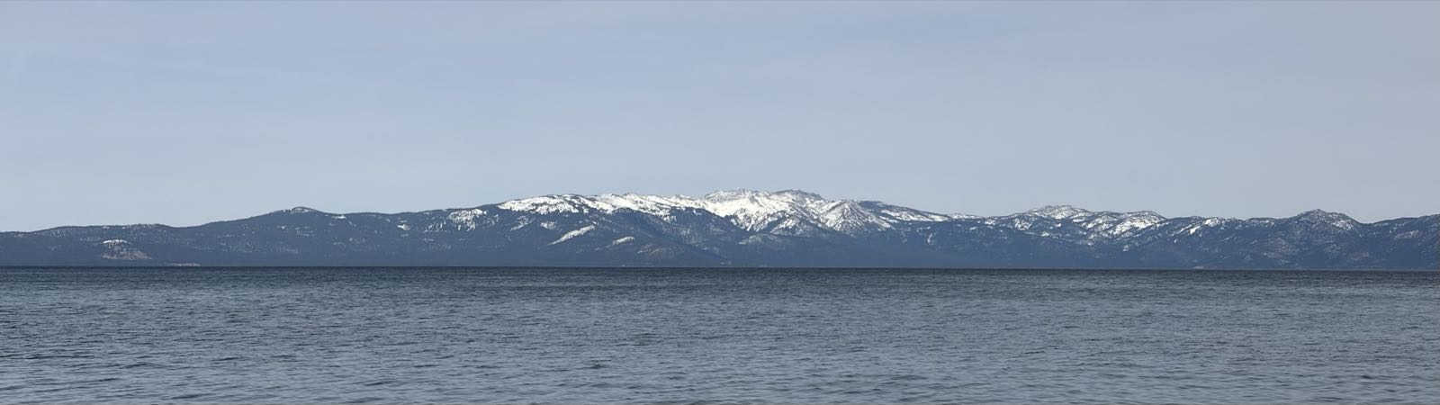 A large body of water is under a clear blue sky. Snow-capped mountains line the far shore.