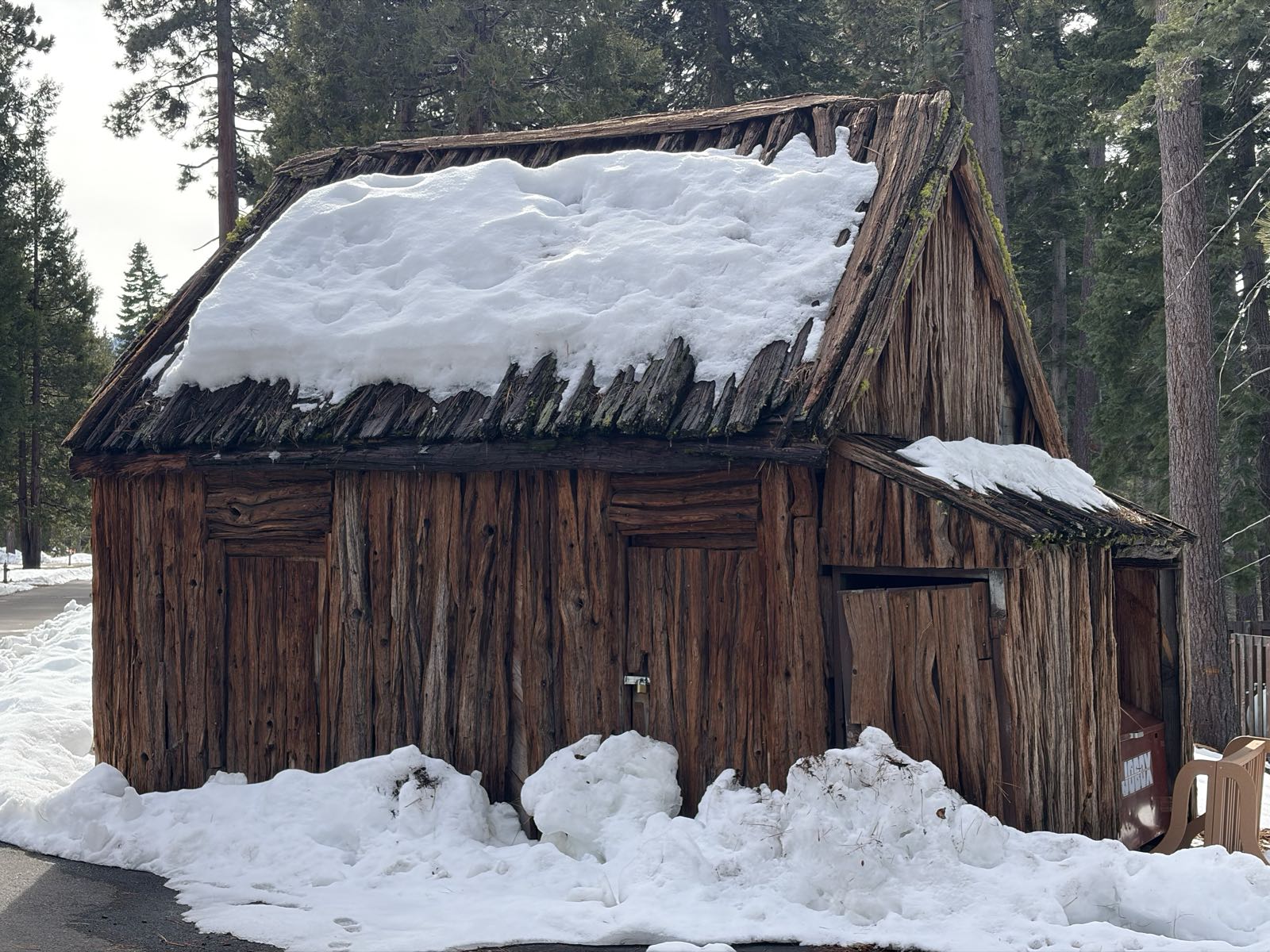 A wooden shed has snow on its roof.