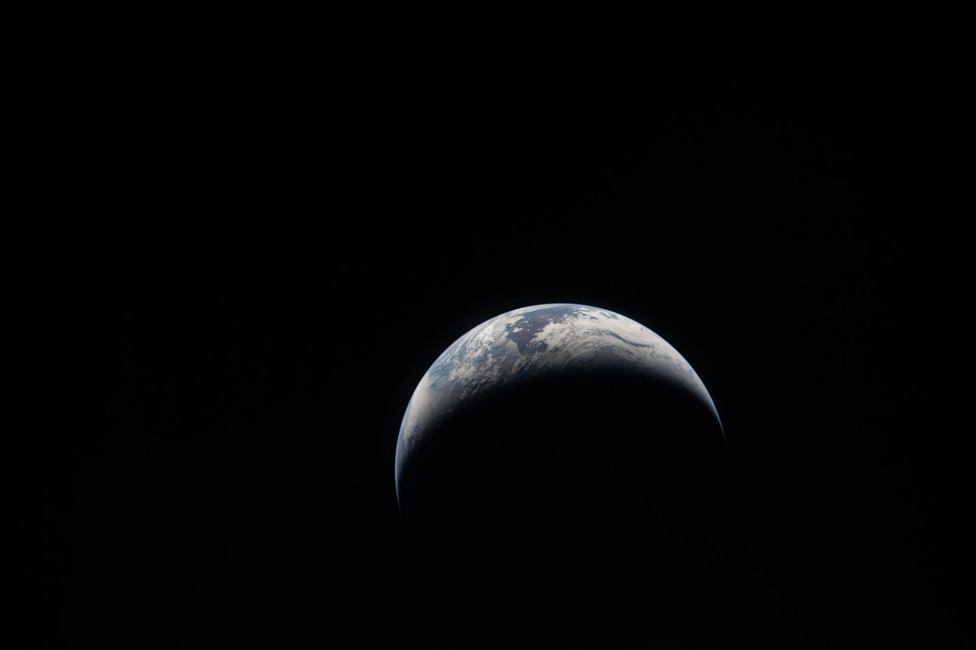 A crescent Earth hangs in the vast blackness of space.