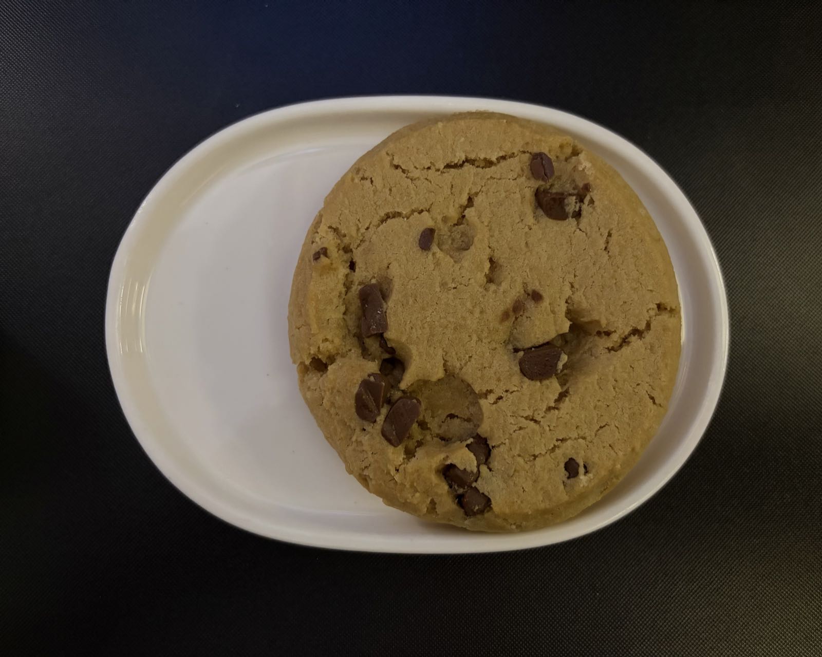 A chocolate chip cookie sits on a lozenge-shaped white plate.