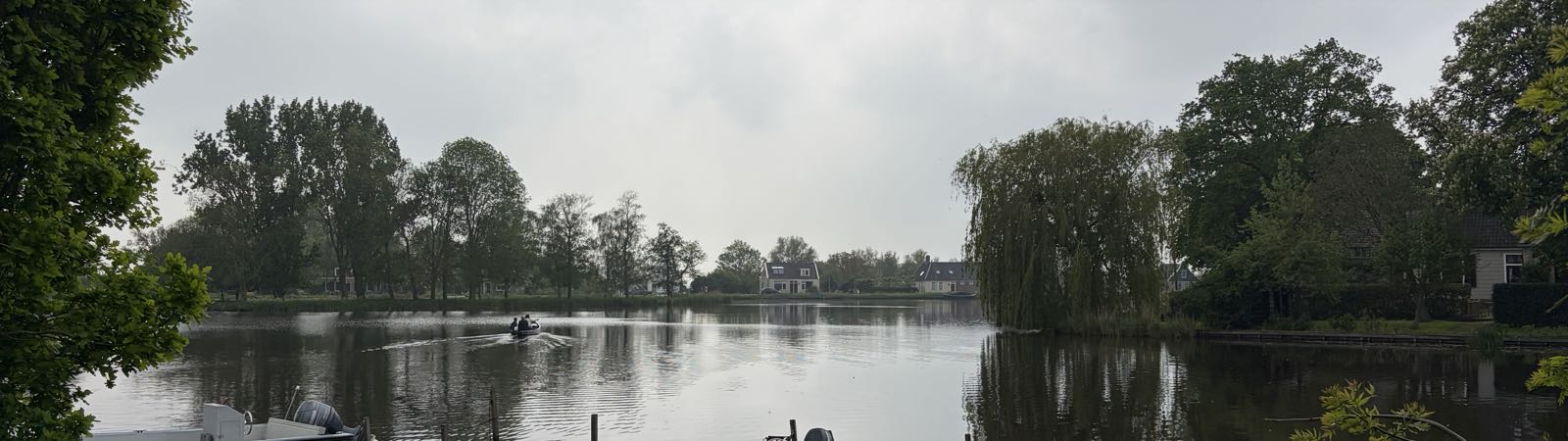 A small motorboat is heading away from the camera, out on a small lake surrounded by trees.