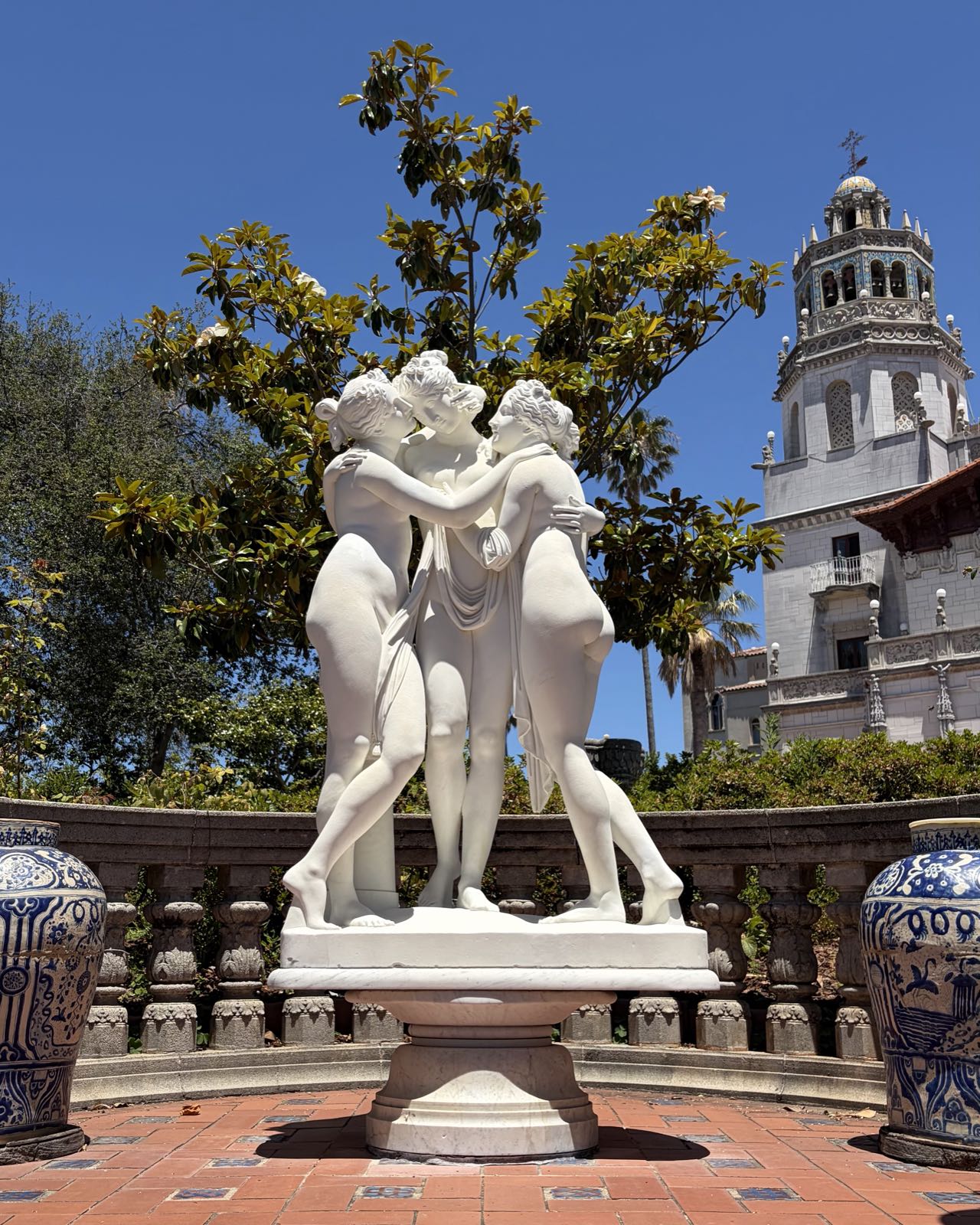 A Grecian-style statue of three women embracing stands in front of a building in the style of a Spanish cathedral.