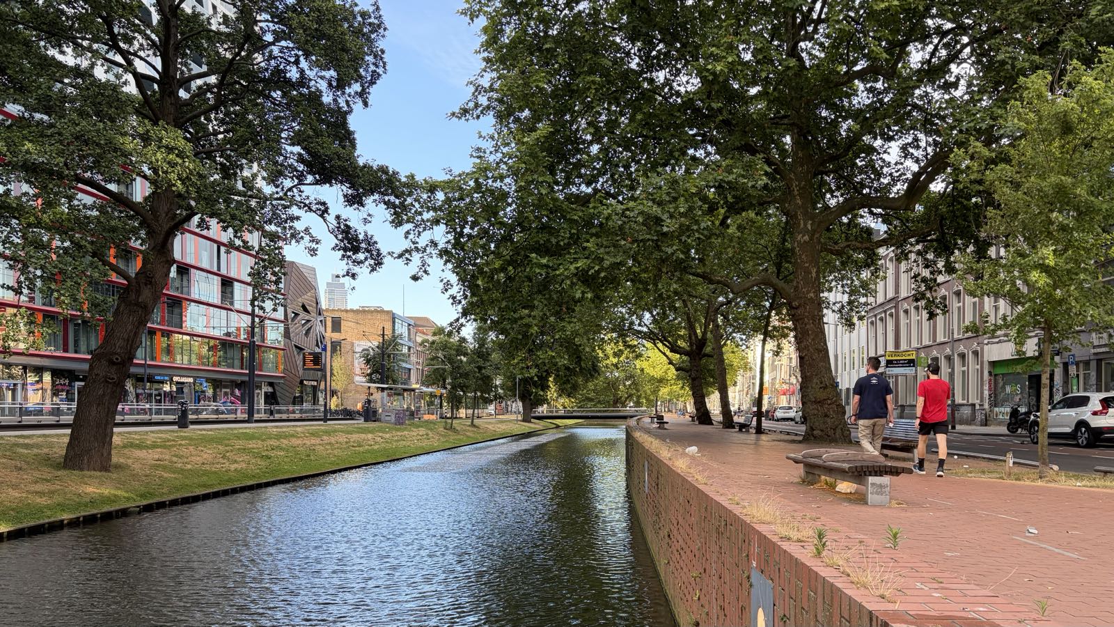 A canal is lined with trees and buildings. The left bank is grassy, and the right is made of brick.