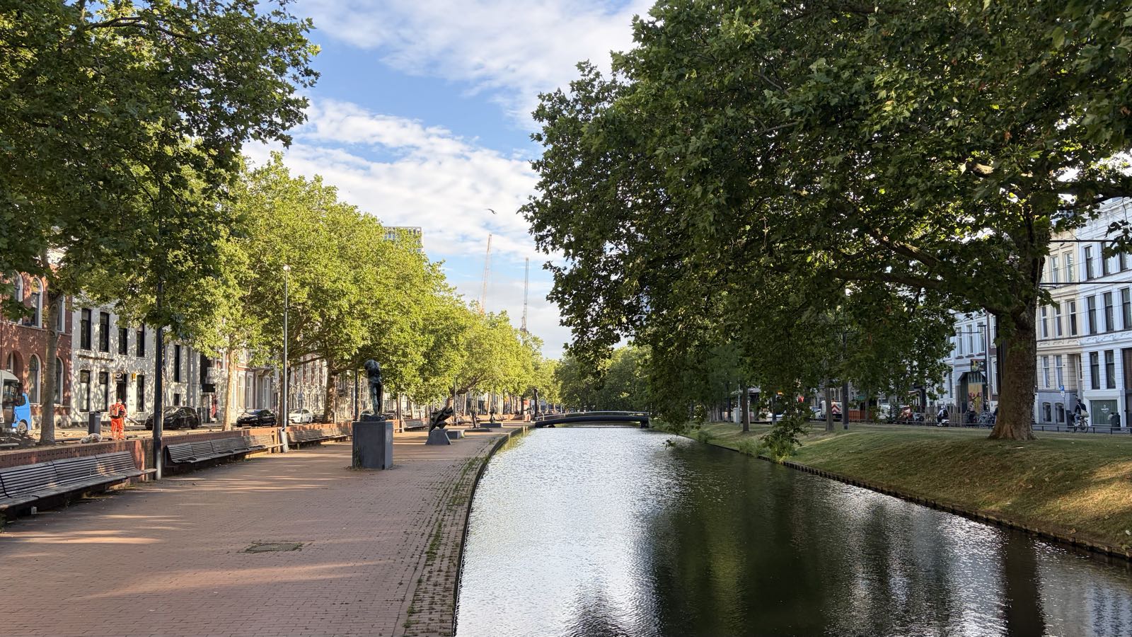 A canal is lined with trees and buildings. The right bank is grassy, and the left is made of brick.