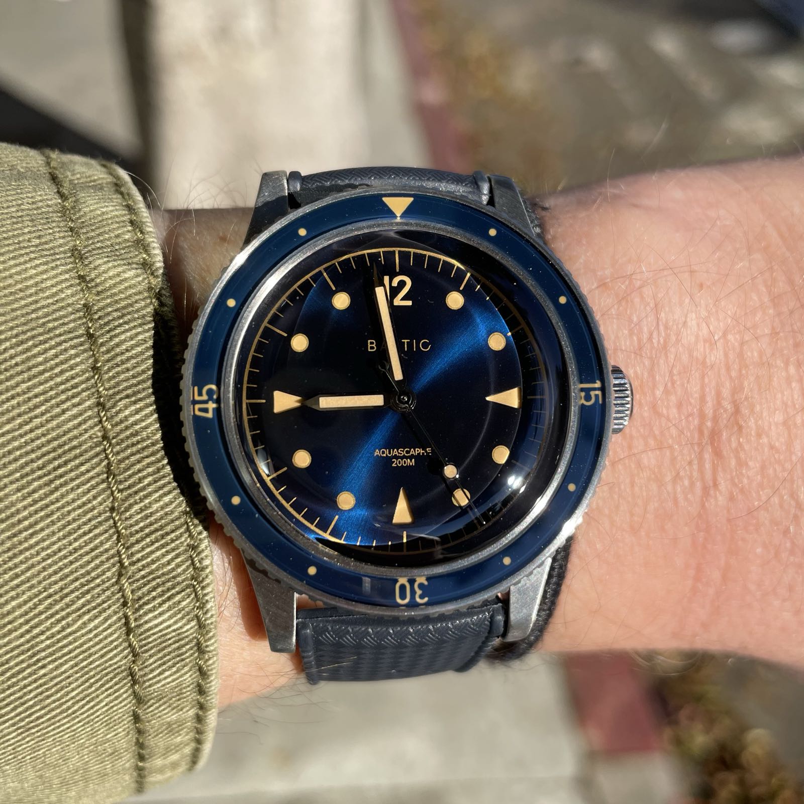 A wrist shot of a stainless steel dive watch. It has a navy blue sunburst dial, a navy blue bezel insert, and faux patina indicies, hands, and bezel markings. It’s on a navy blue tropic rubber strap.