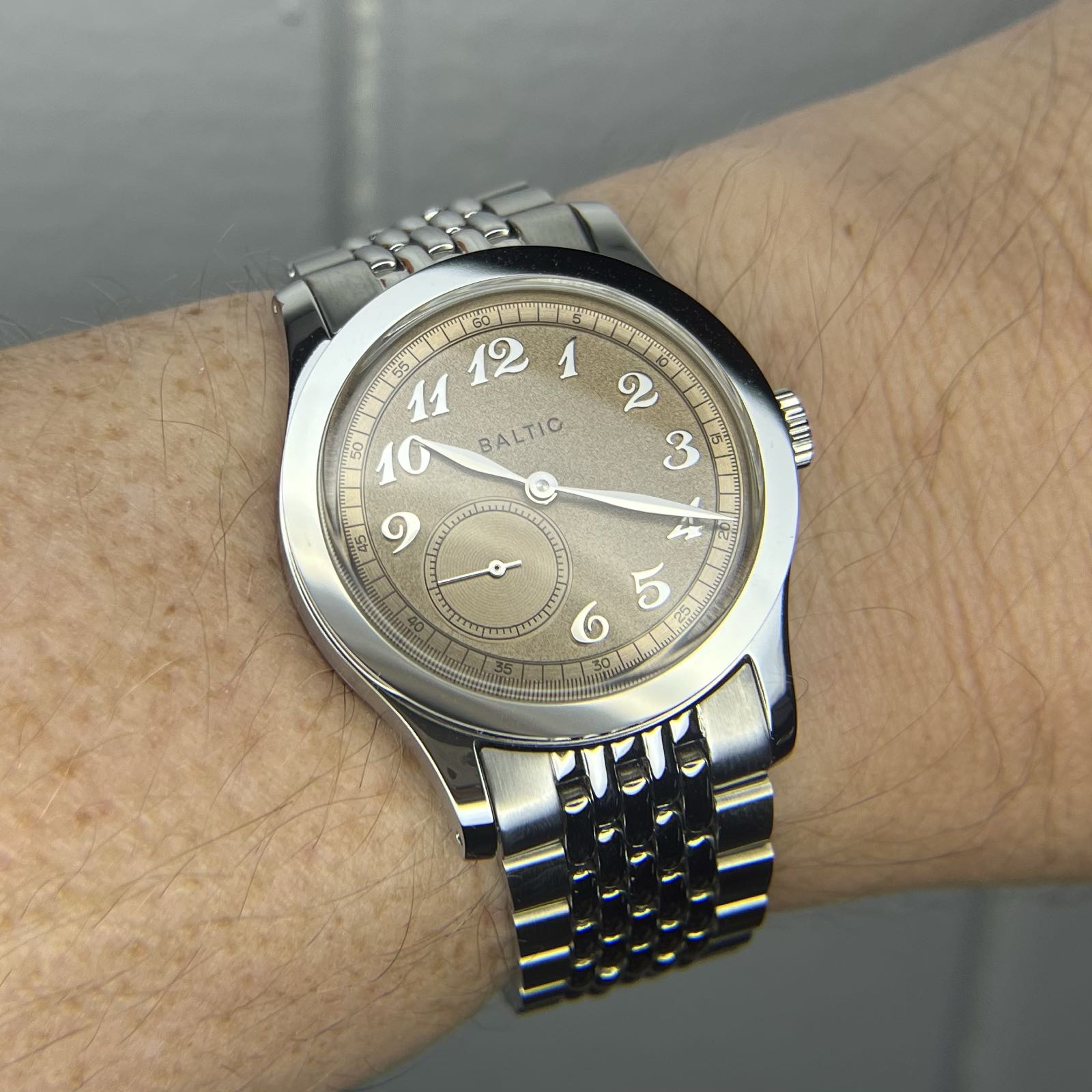 A stainless steel watch on a beads of rice bracelet. The dial is salmon-colored, with Breguet numerals. There’s a subdial at 7:30 with the running seconds hand.