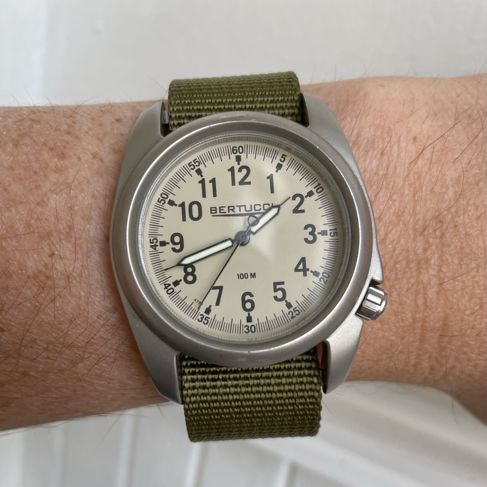 A field watch on an olive-green nylon strap. The crown is at 4:00. The dial is cream-colored, with very legible black arabics at the hours.
