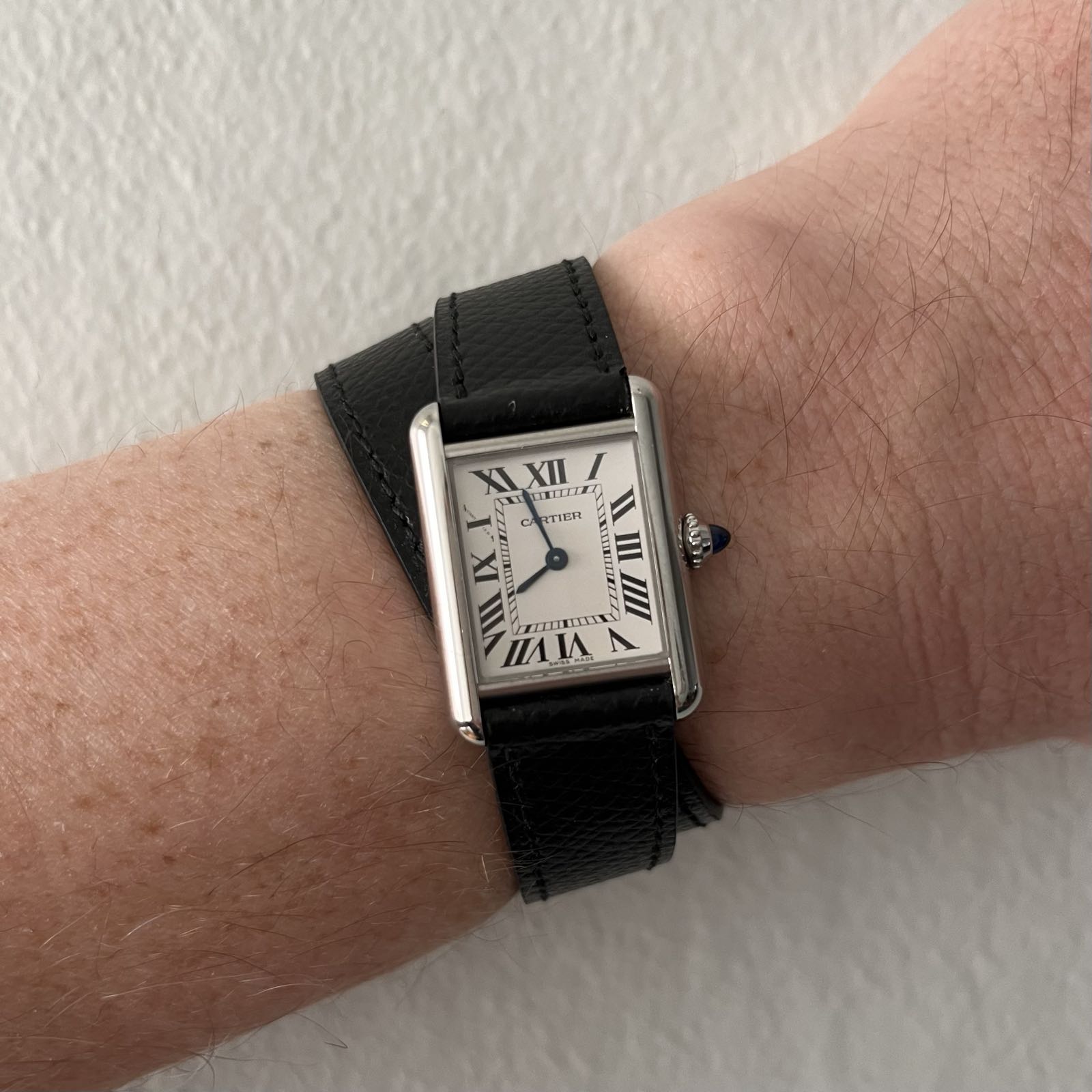 A stainless steel, rectangular dress watch. The dial is white, with black Roman numerals for hour markers. The hands are blued. It’s on a double tour black leather strap.