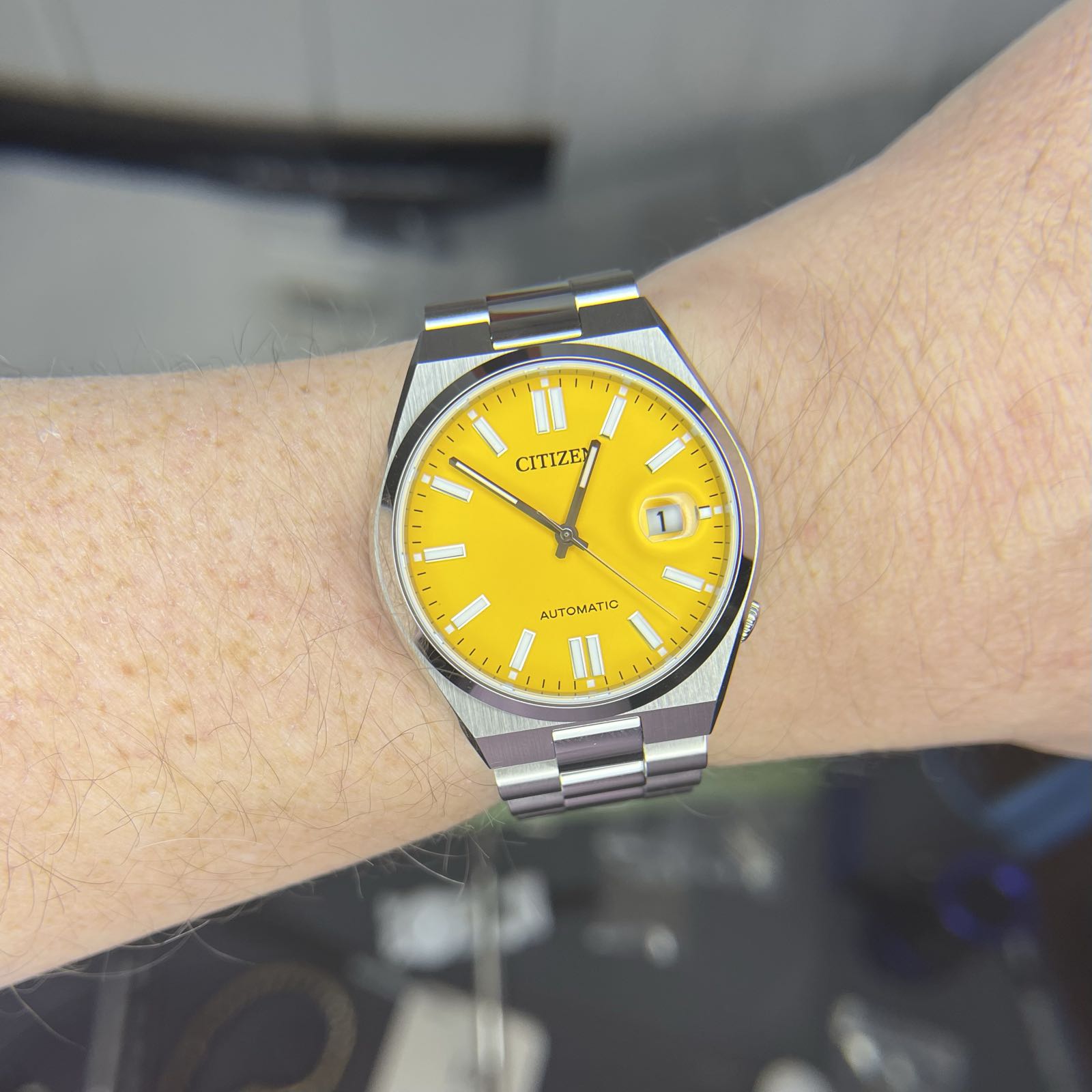 A steel sports watch with a bright yellow face. Simple stick hour markers and hands. There’s a cyclops at 3:00 to help read the date complication.