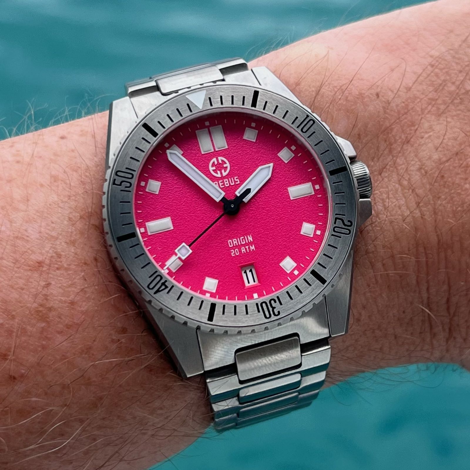 A steel watch is center frame, with a bright pink dial with white hands and indices, an aluminum, rotating, dive-time bezel, and an H-link bracelet.