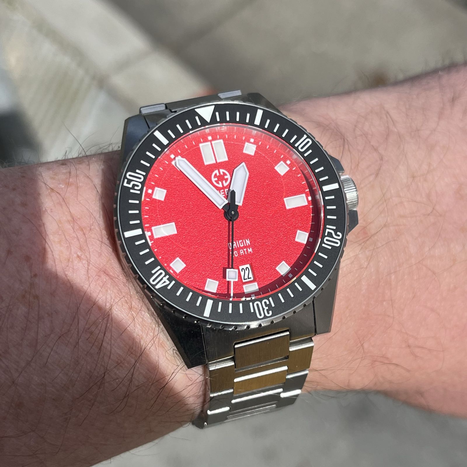 A steel watch is center frame, with a bold red dial with white hands and indices, a black, rotating, dive-time bezel, and an H-link bracelet.