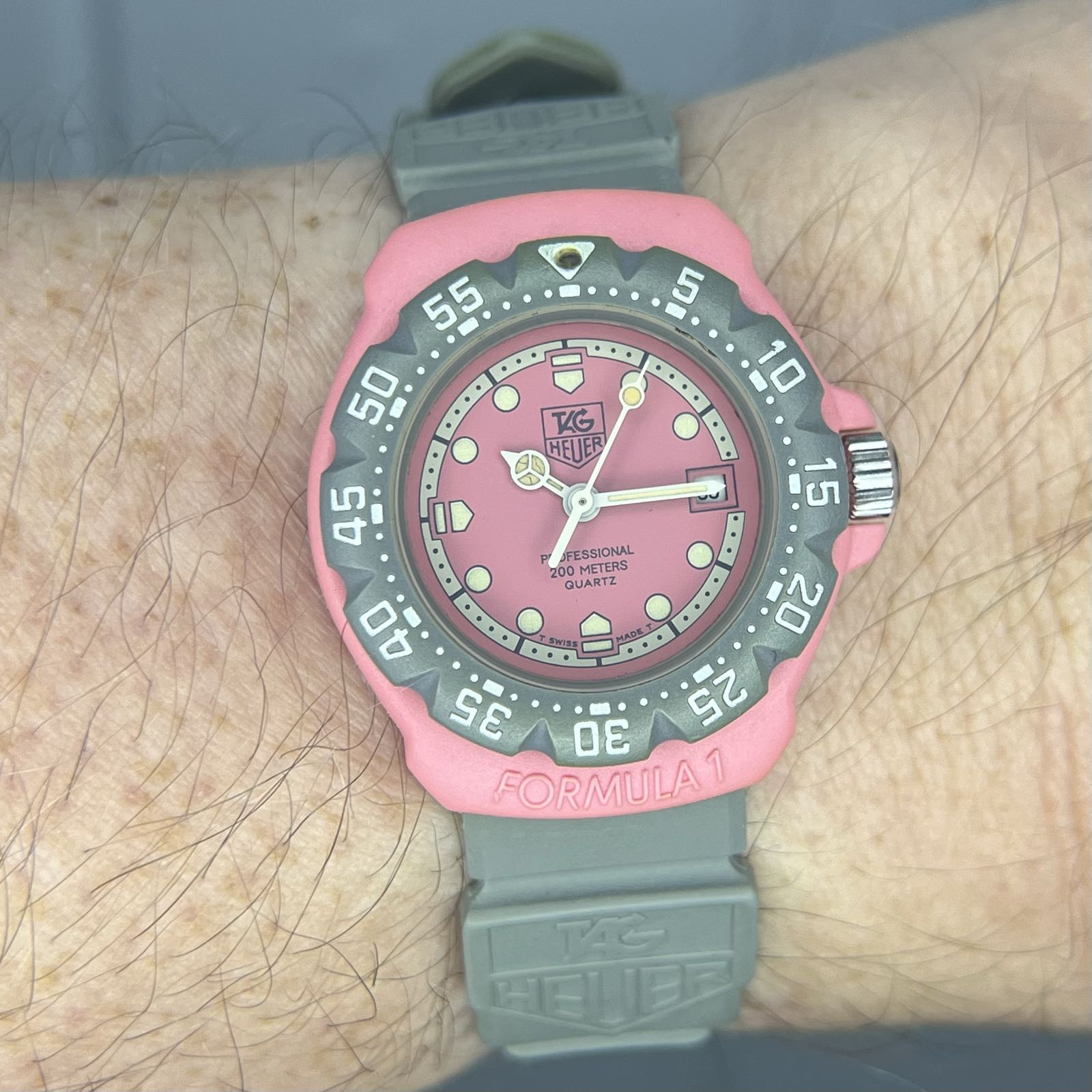 A wrist shot of a small, plastic watch.
It’s got a pink case and dial, and a gray bezel and strap.