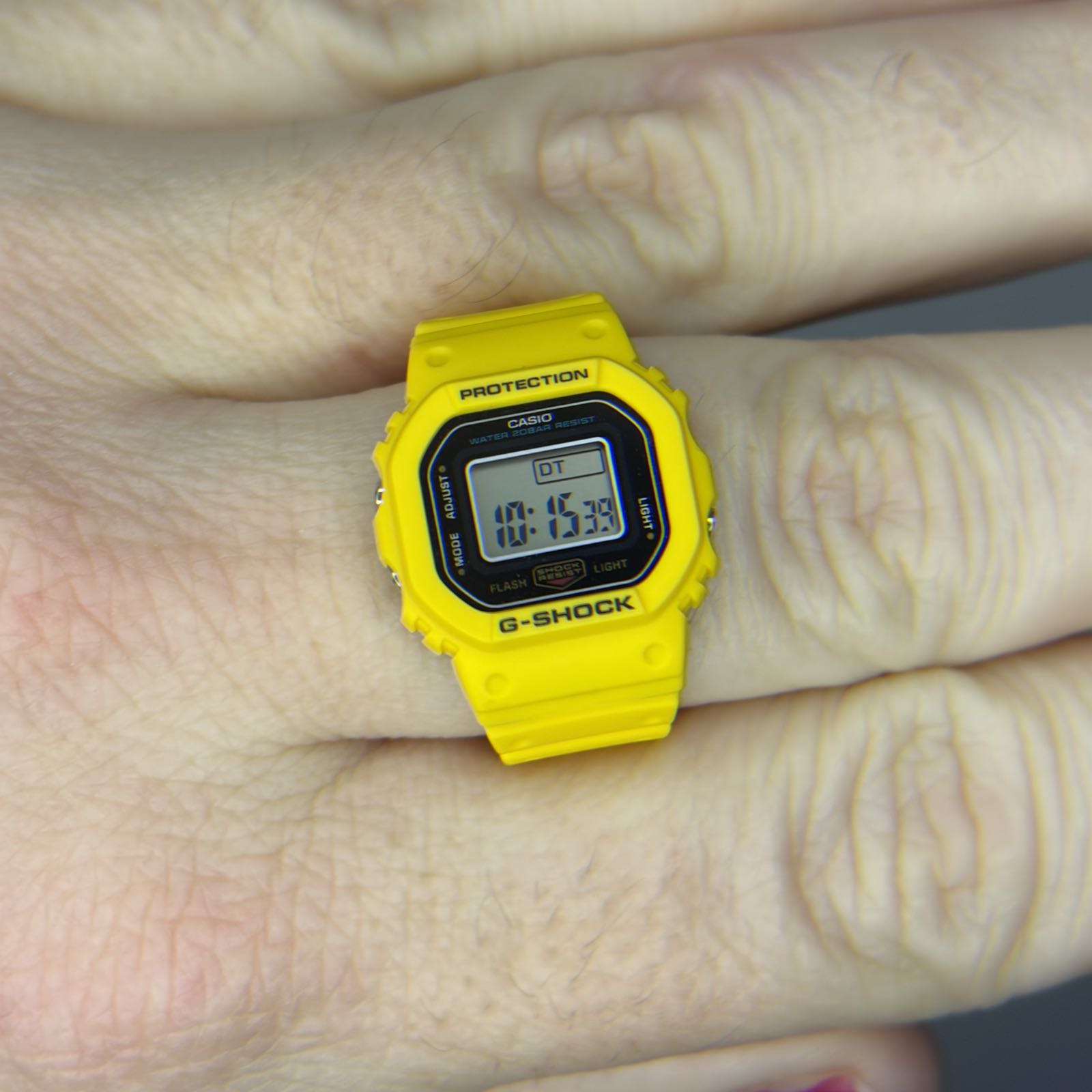 A yellow plastic digital ring watch with a black dial surrounding a positive display.