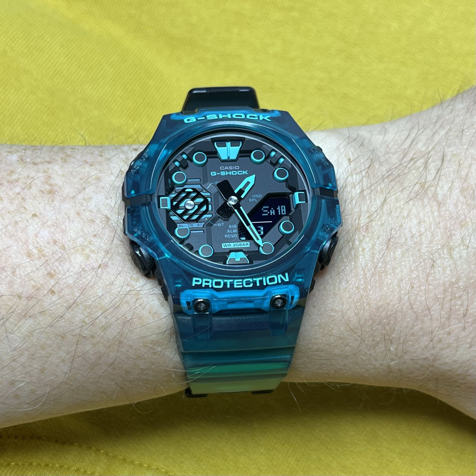 A turquoise plastic analog/digital watch. The display is black. The hour markers, hands, and several other elements on the dial have parts in the same turquoise as the case and band.