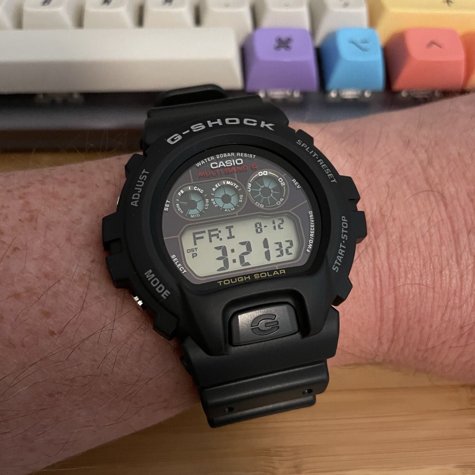 A black plastic digital watch with a black dial. There are four positive displays: three circular displays in a row at the top, and a date and time readout at the bottom. Below the dial is a large black button with a G in the middle.