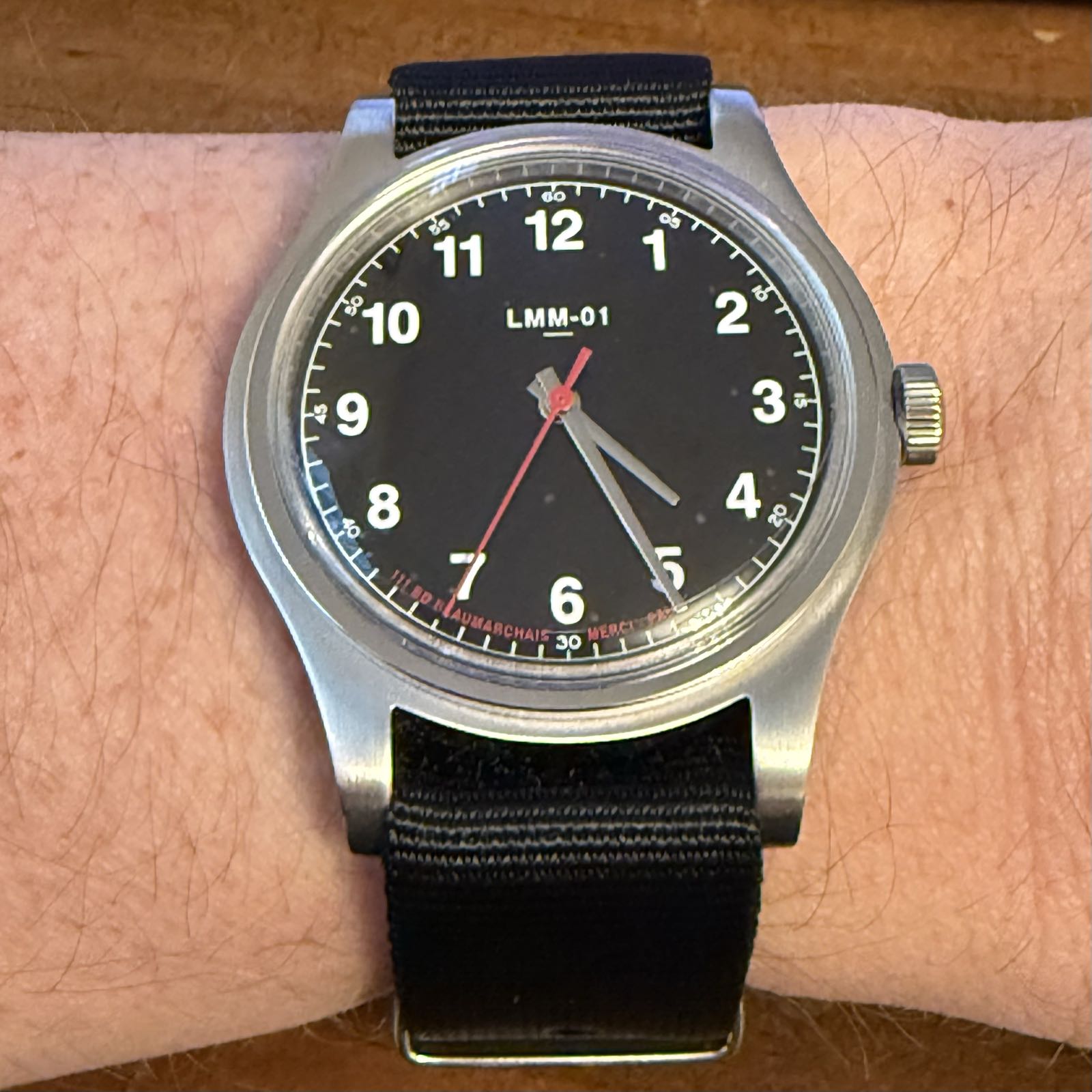 A simple watch on a black strap. It has a black dial, with white Arabic numerals as hour markers. The seconds hand is red.
