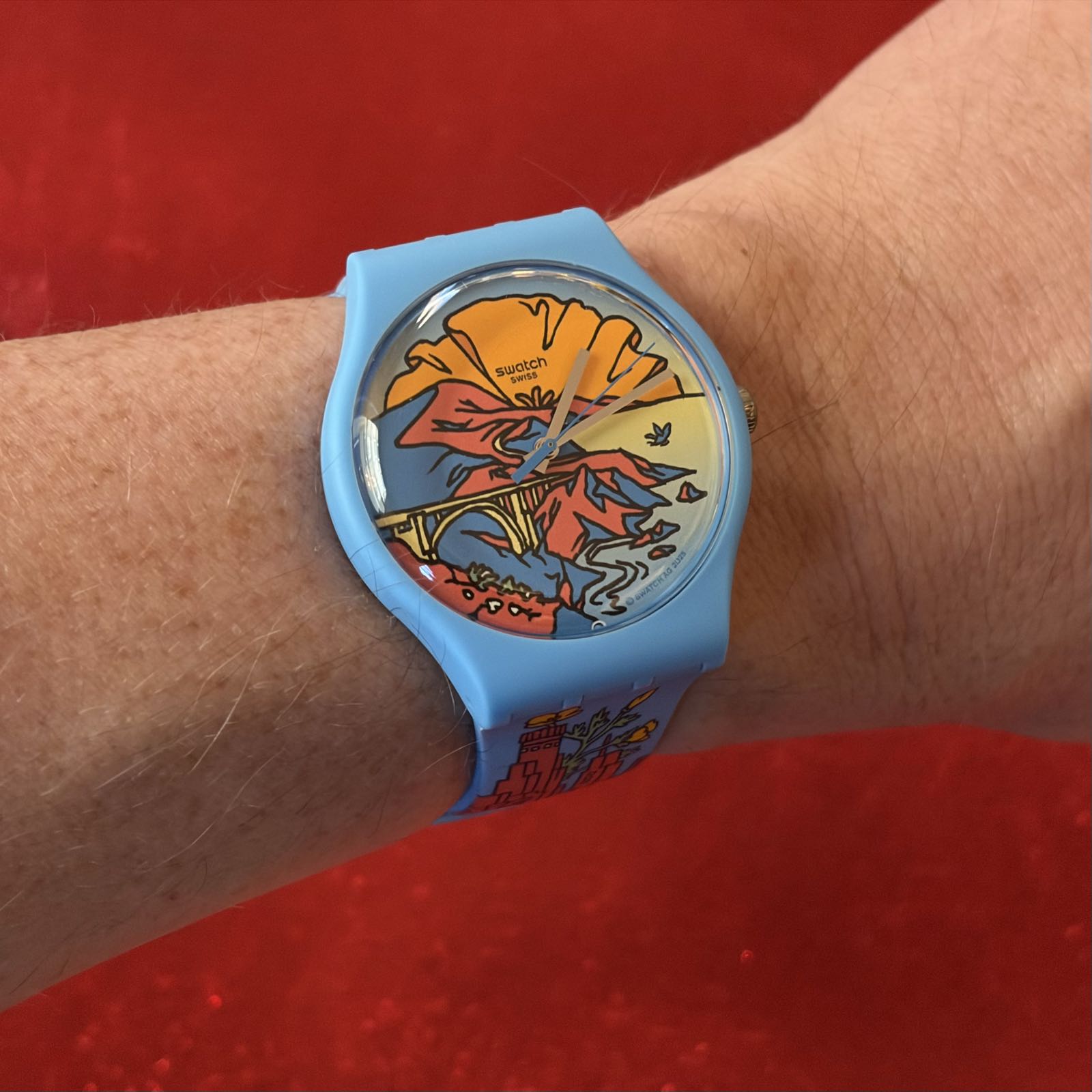 A blue watch with red and orange art on it is on someone’s wrist.